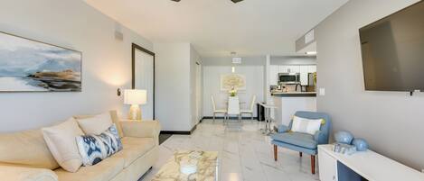 A modern living room with a sofa, coffee table, and a dining area in the background.
