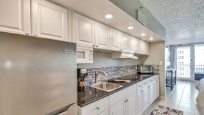 Una cocina moderna con armarios blancos, un lavamanos de acero inoxidable y un microondas integrado.