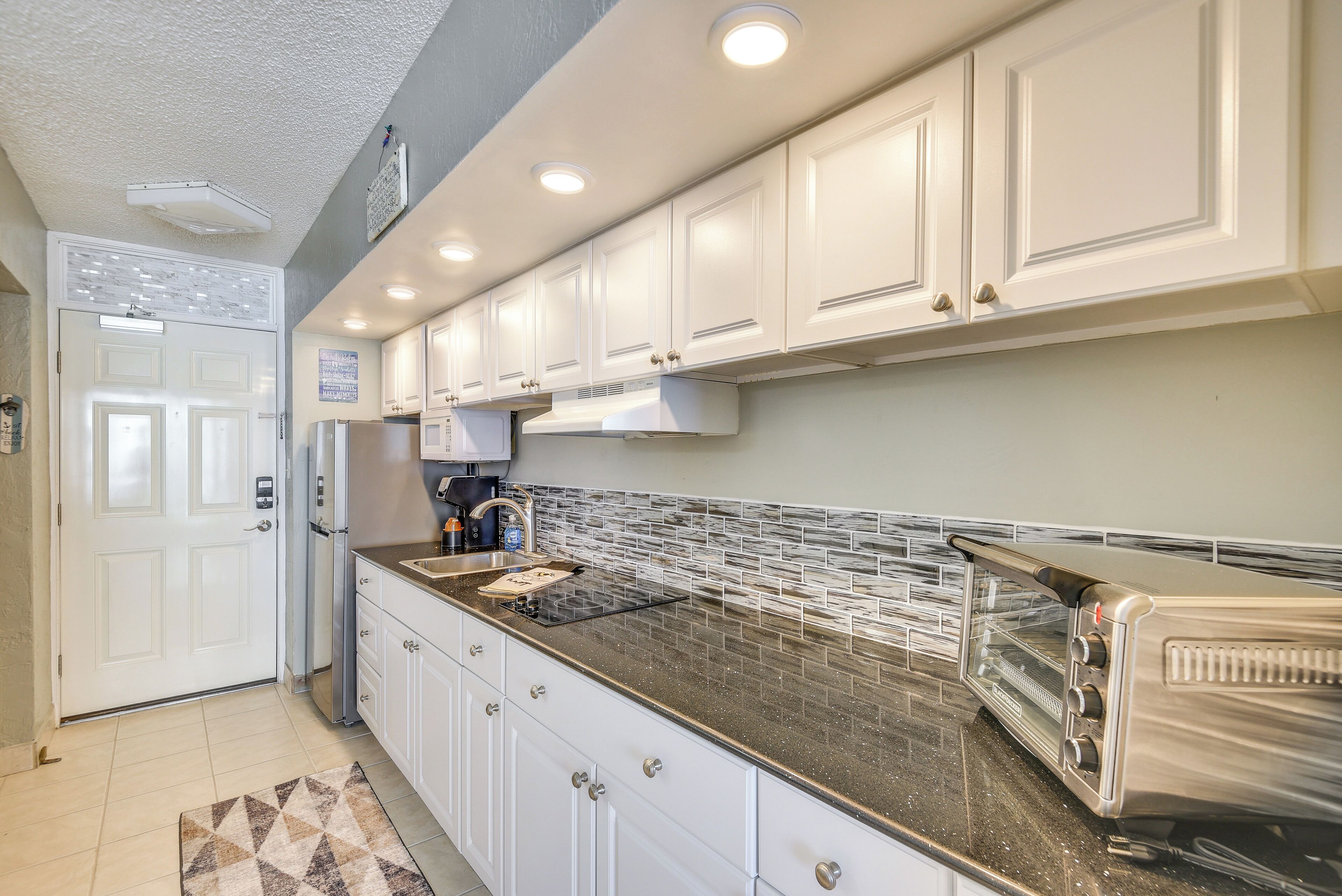 A modern kitchen with white cabinets, a stainless steel toaster, and a patterned backsplash.