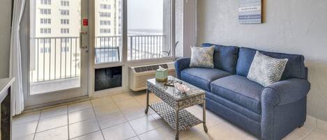 A living room with a blue sofa, a glass coffee table, and a ceiling fan.