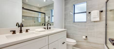 A modern bathroom with a double sink vanity, a large mirror, and a glass shower enclosure.