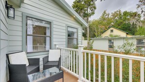 A covered porch with wicker furniture and a glass table, white railings, and a view of neighboring houses.