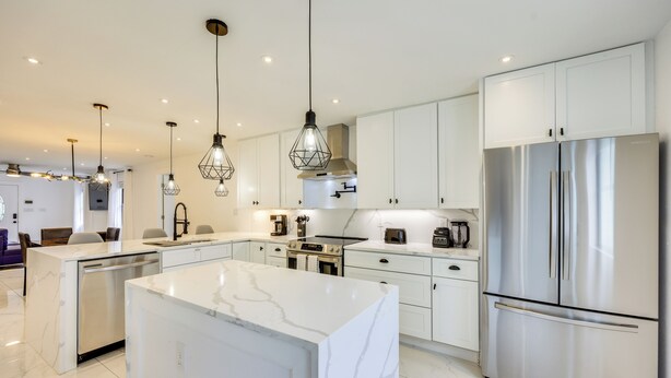 A modern kitchen with white cabinetry, stainless steel appliances, and pendant lighting.