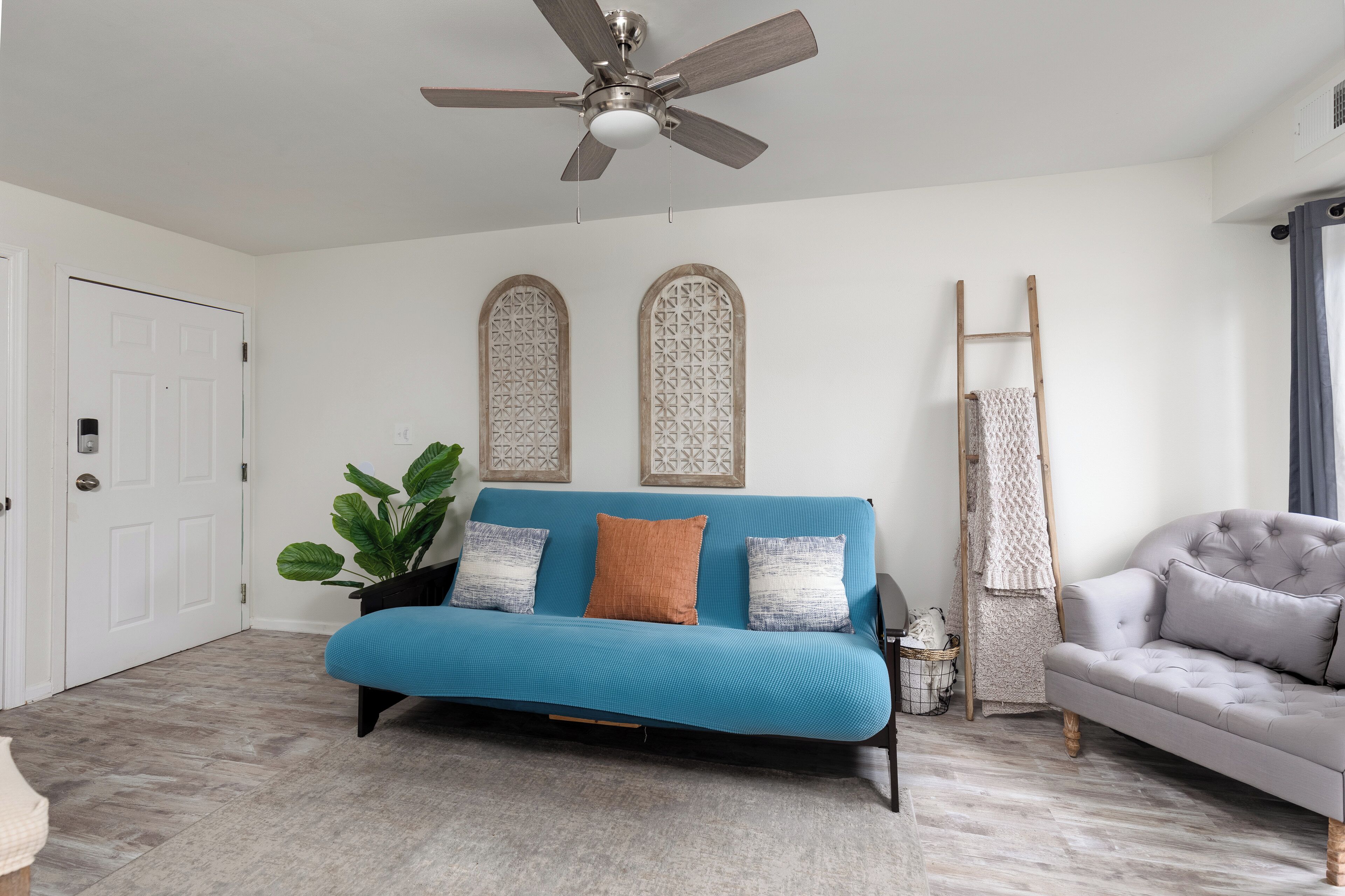 A room with a blue sofa, a grey armchair, a ceiling fan, and a white door.