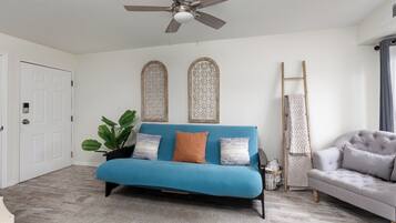A room with a blue sofa, a grey armchair, a ceiling fan, and a white door.