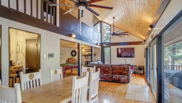 A spacious dining area with a wooden table and white chairs, a leather sofa, and a ceiling fan. - Ruidoso Cabin Retreat w/ Multi-level Deck (Ruidoso)
