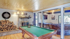 A pool table in a room with wooden flooring, a dartboard, and a stone wall. - Ruidoso Cabin Retreat w/ Multi-level Deck (Ruidoso)