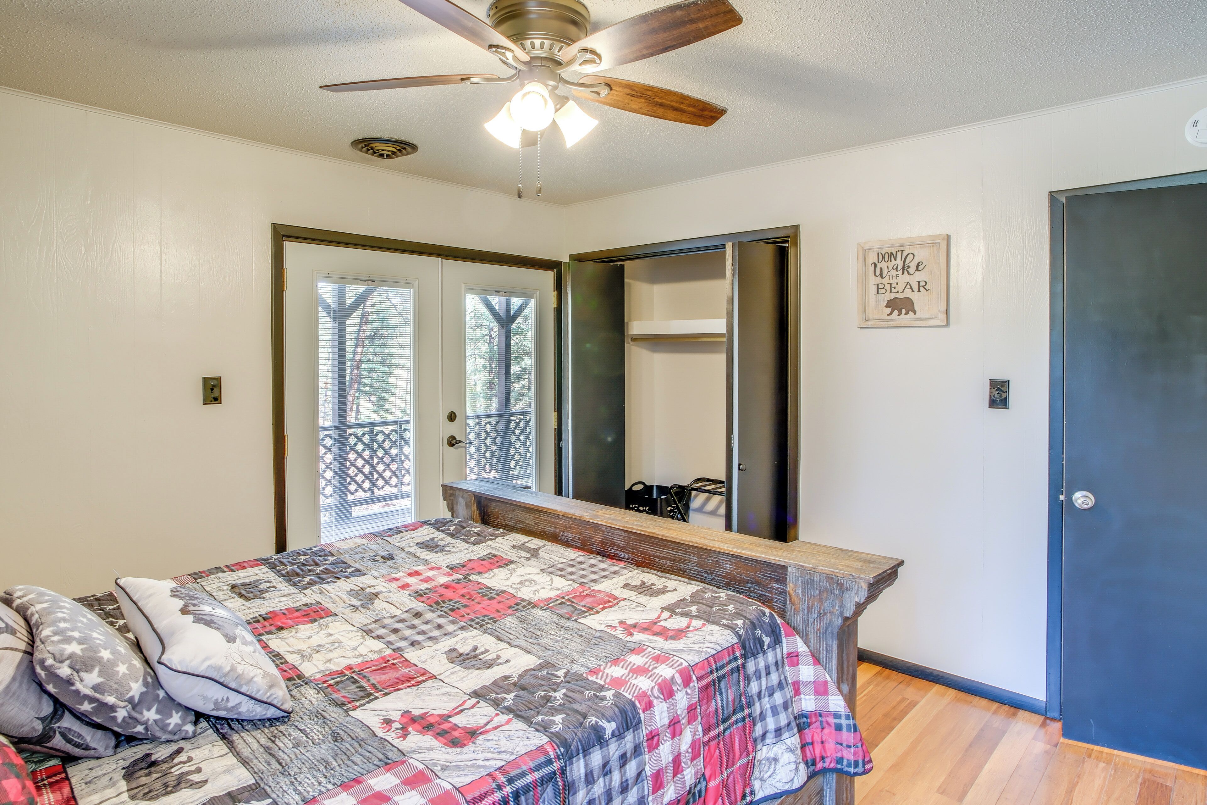 A bedroom with a bed, a ceiling fan, a window, a door, and a mirror.