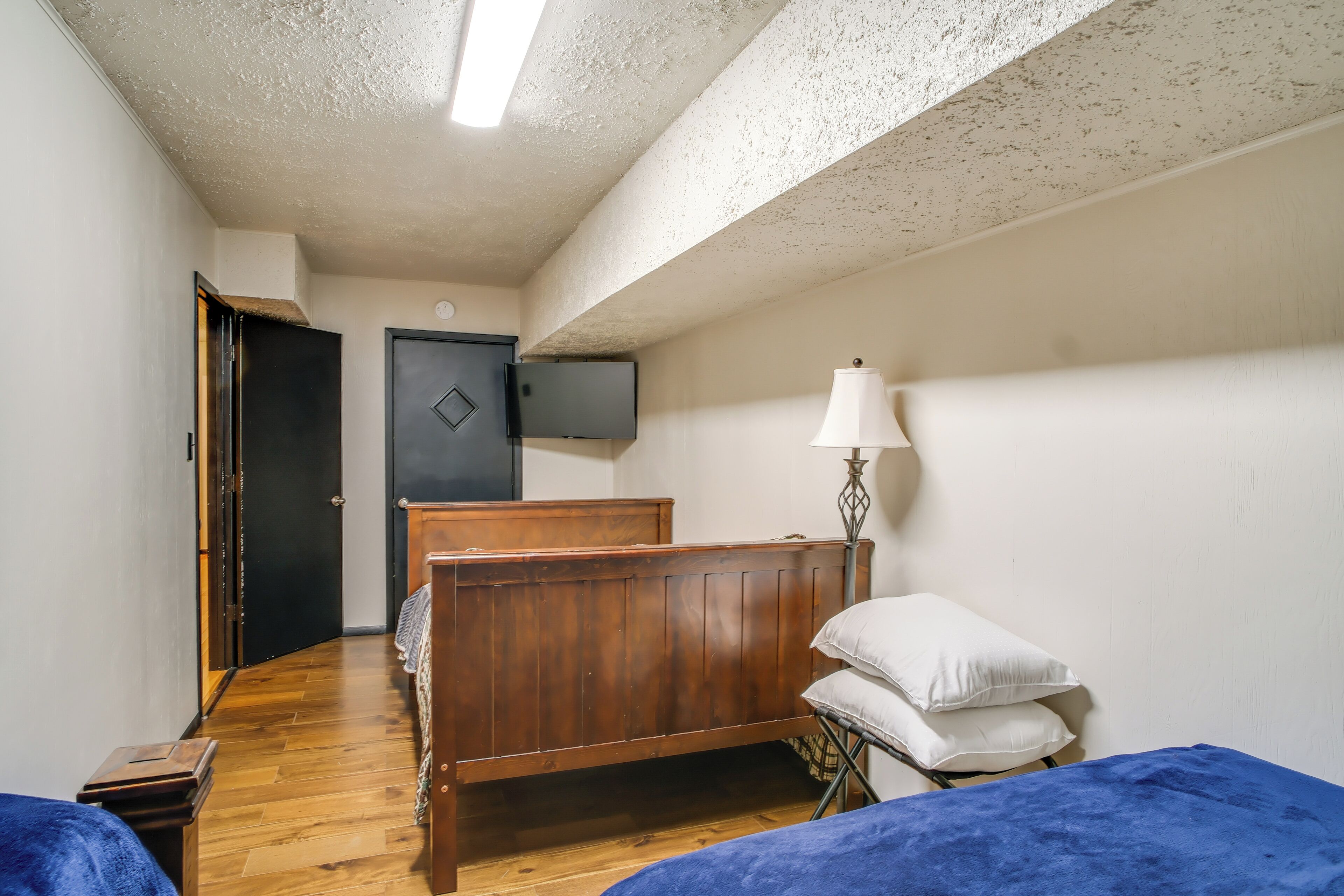 Quarto com cama de madeira, luminária de cabeceira e televisão na parede.
