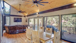 A spacious living area with a wooden ceiling, large windows, a TV, and a dining table with chairs. - Ruidoso Cabin Retreat w/ Multi-level Deck (Ruidoso)