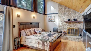 A bedroom with a wooden bed, stone wall, and a fireplace. - Ruidoso Cabin Retreat w/ Multi-level Deck (Ruidoso)