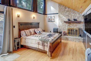 A bedroom with a wooden bed, stone wall, and a fireplace. - Ruidoso Cabin Retreat w/ Multi-level Deck (Ruidoso)