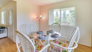 Een eethoek met een ronde tafel voor vier personen, omringd door witte rieten stoelen met bloemkussentjes.