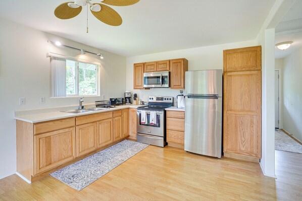 A modern kitchen with wooden cabinets, stainless steel appliances, and a large window. - Captain Cook Home on Quiet 3 Acres w/ Fruit Trees (Captain Cook)