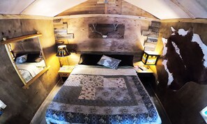 A rustic wooden room with a bed, a nightstand, a lamp, and a wall-mounted shelf.