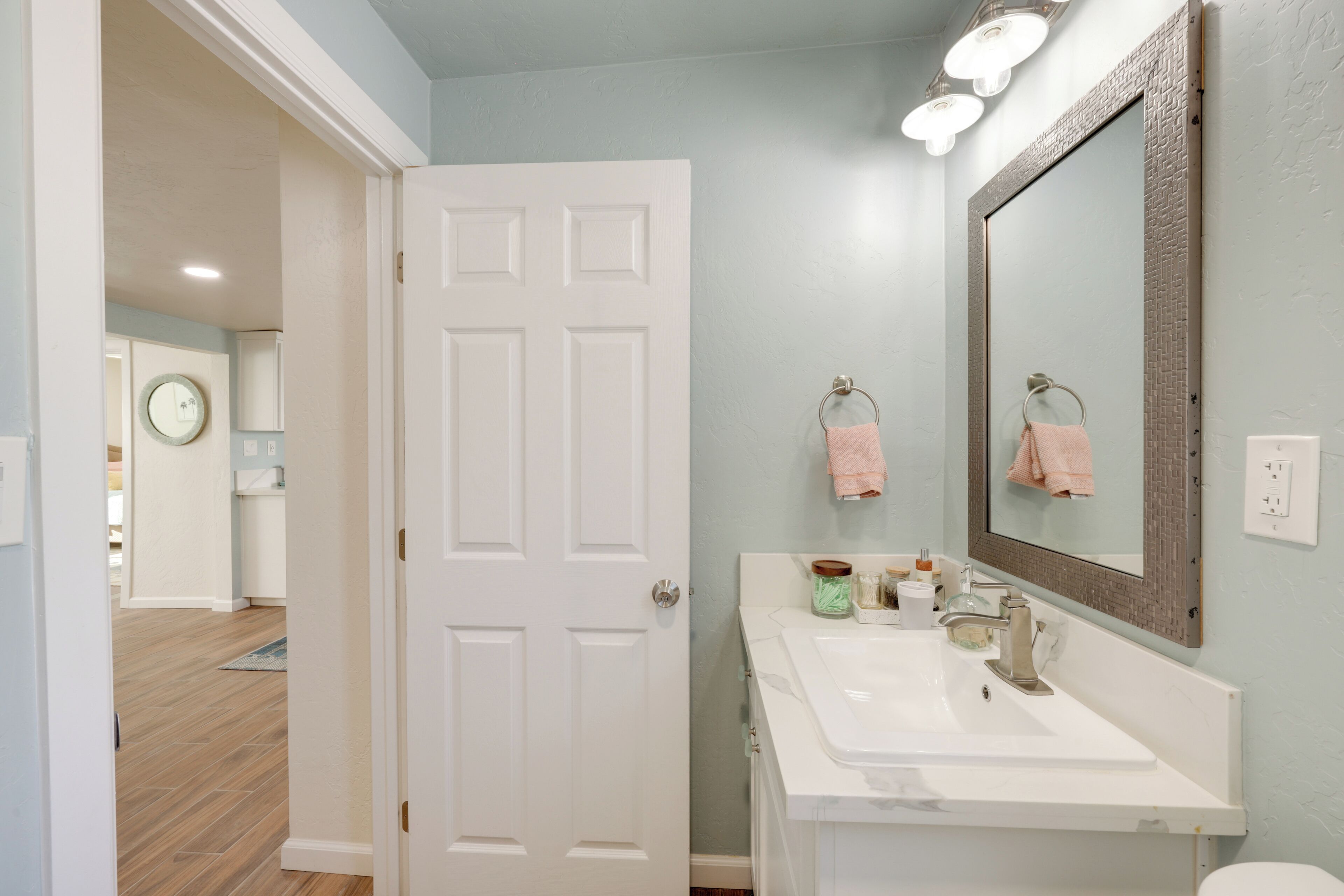 Une salle de bain avec une porte blanche, un lavabo avec un miroir et un porte-serviettes avec des serviettes roses.