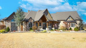 A large, multi-story stone house with a prominent front porch, multiple chimneys, and a well-maintained lawn. - Spacious Owasso Vacation Rental w/ Private Pool! (Owasso)