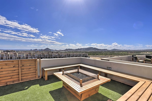 A rooftop terrace with a wooden deck, a fire pit, and a view of the cityscape and mountains.