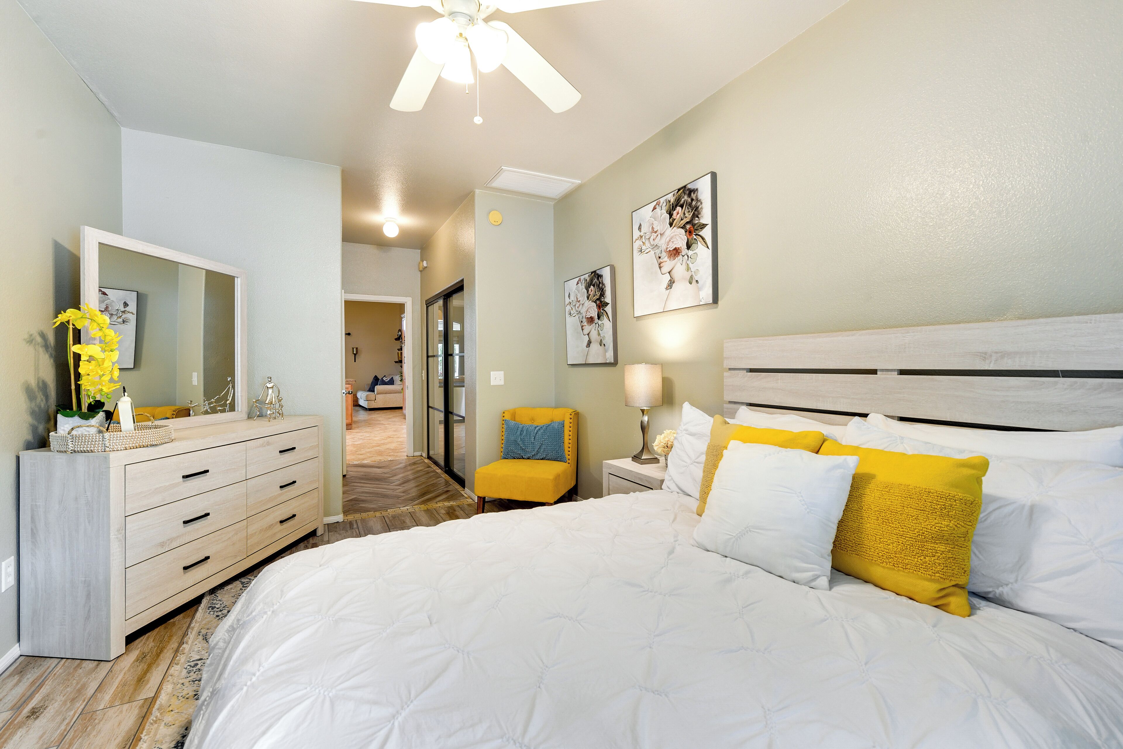 A bedroom with a bed, a dresser, a chair, and artwork on the wall.