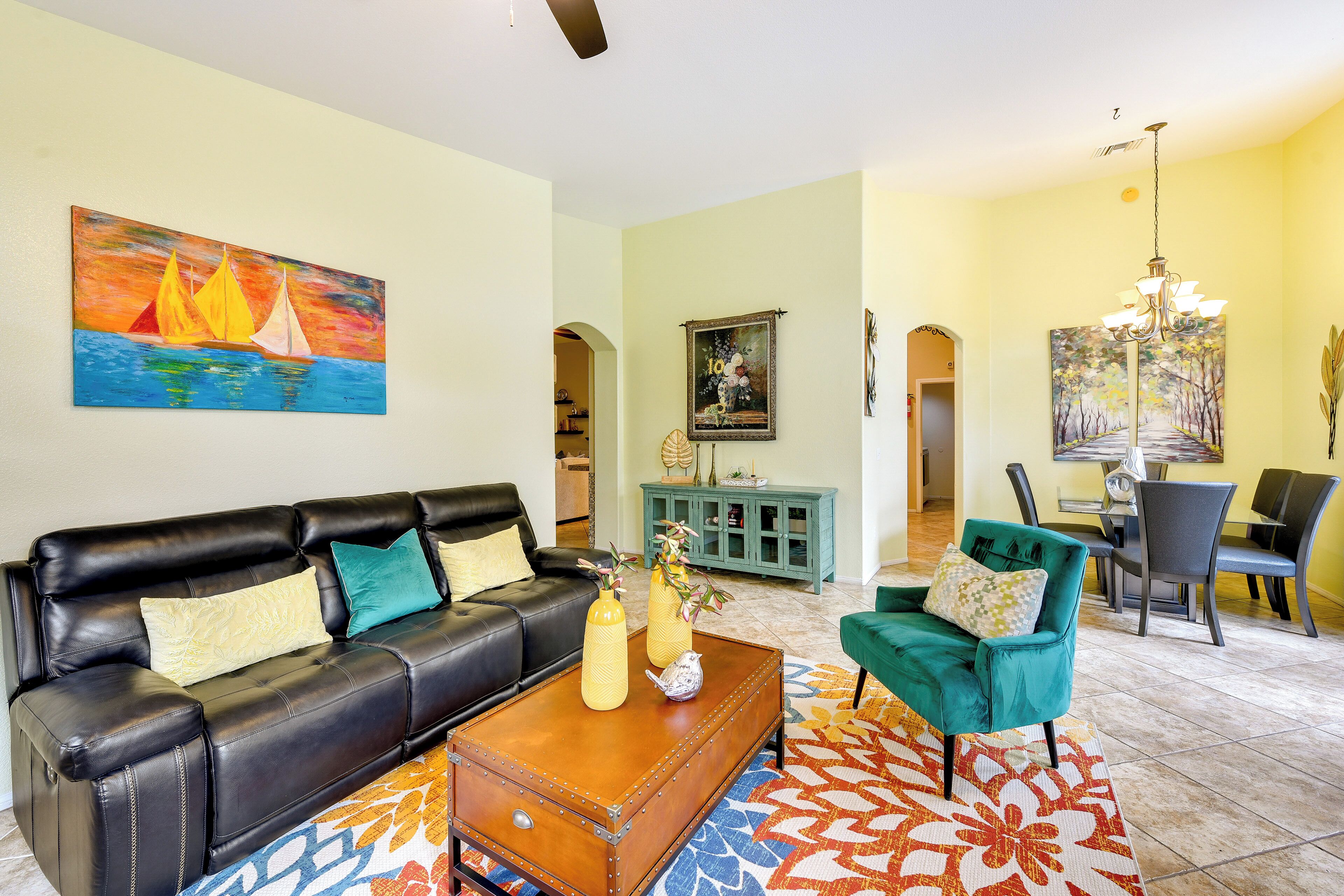 Un salon avec un canapé en cuir noir, une table basse et un fauteuil turquoise. Un tableau est accroché au mur, et un lustre est suspendu au plafond.