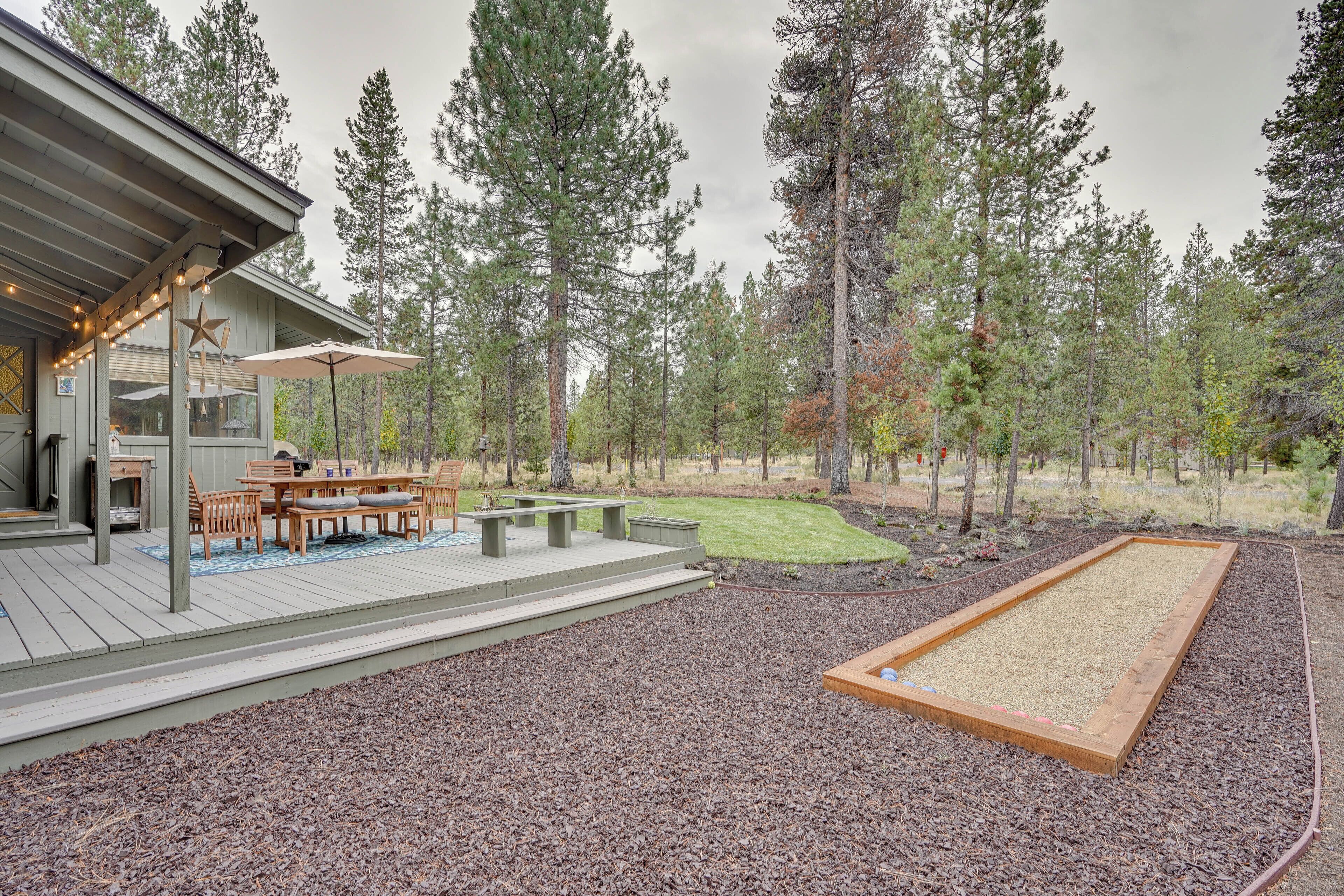 Une terrasse dotée de mobilier d’extérieur, d’un foyer et d’un espace jardin entouré de grands arbres.