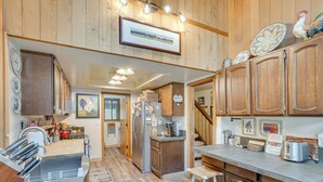 A kitchen with wooden cabinets, a stainless steel refrigerator, and a bar area with stools. - Sunriver Resort Home: Near Skiing, Town & Trails (Bend)