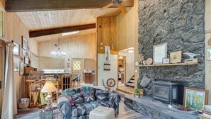 A cozy cabin interior with a stone fireplace, wooden walls, a dining area, and a living room with a patterned sofa and ottoman. - Sunriver Resort Home: Near Skiing, Town & Trails (Bend)