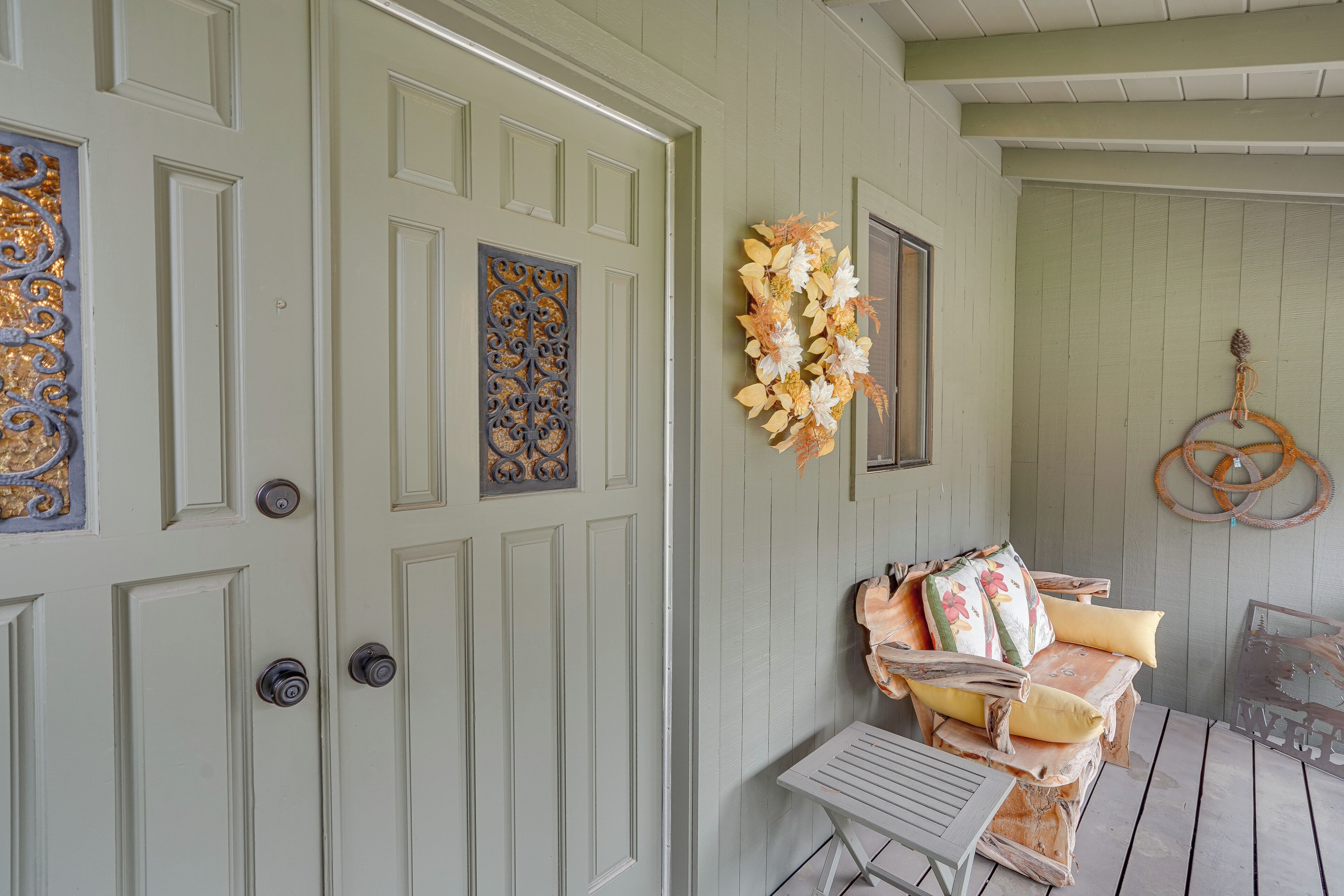 A room with a light green door, a decorative wreath, and a rustic bench with cushions.