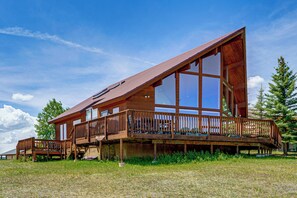 Uma cabana moderna de madeira com um deck espaçoso, grandes janelas e telhado inclinado.