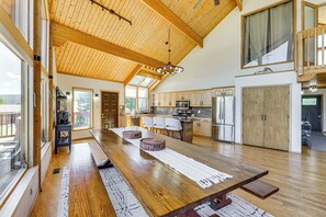 Cozinha espaçosa com vigas de madeira, uma mesa de jantar comprida e vista para o exterior.