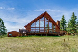 Une cabane en bois dotée d’une grande terrasse, entourée d’un champ verdoyant et d’arbres.