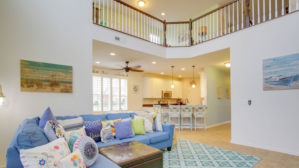 A spacious living room with a blue sectional sofa, a patterned rug, and a dining area with a white table and chairs. - Shuttle to Beach: Millville Townhome w/ Porch (Millville)