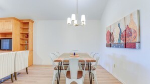 Un coin repas avec une table en bois, des chaises blanches, un lustre et un tableau au mur.