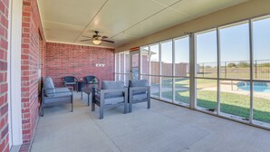 Un patio couvert avec un mur en briques, un ventilateur de plafond et une vue sur une cour arrière avec une piscine.