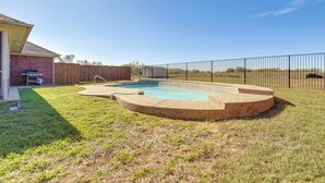 Un jardin avec une piscine, une clôture en bois et une maison en briques.
