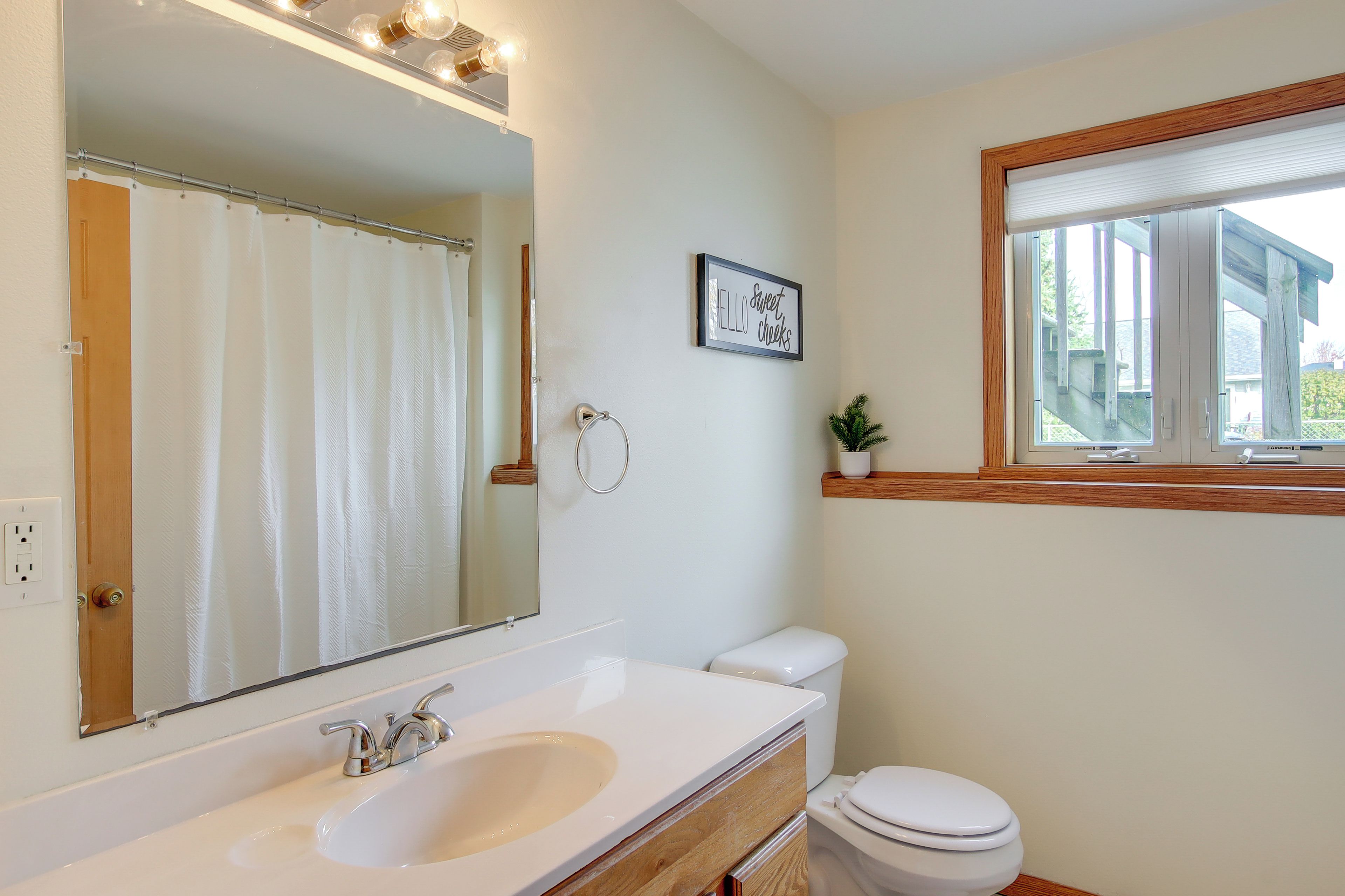 A bathroom with a white sink, a mirror, a toilet, and a window with a view of the outside.