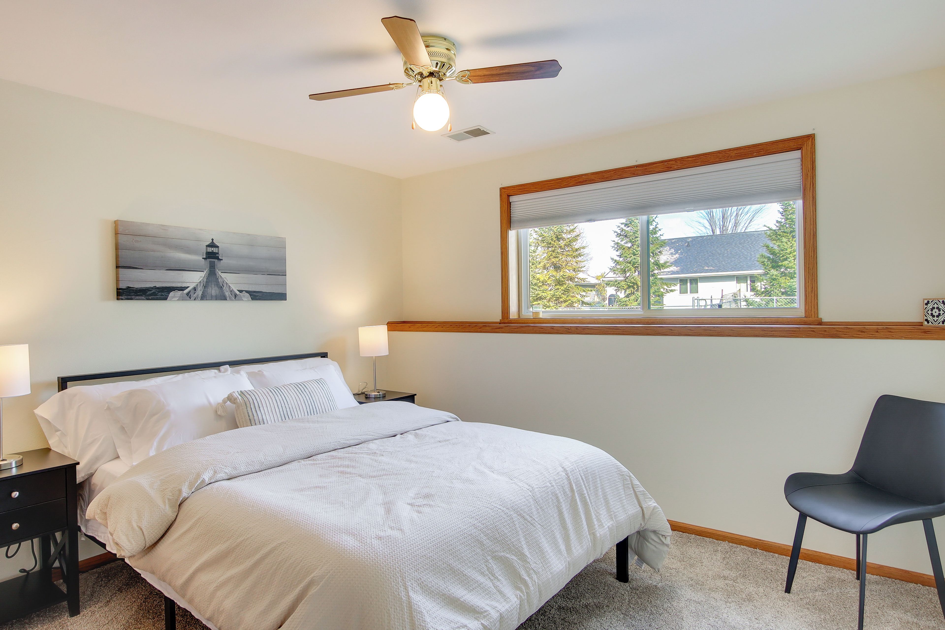 A bedroom with a bed, a chair, a ceiling fan, a window with blinds, and a painting on the wall.