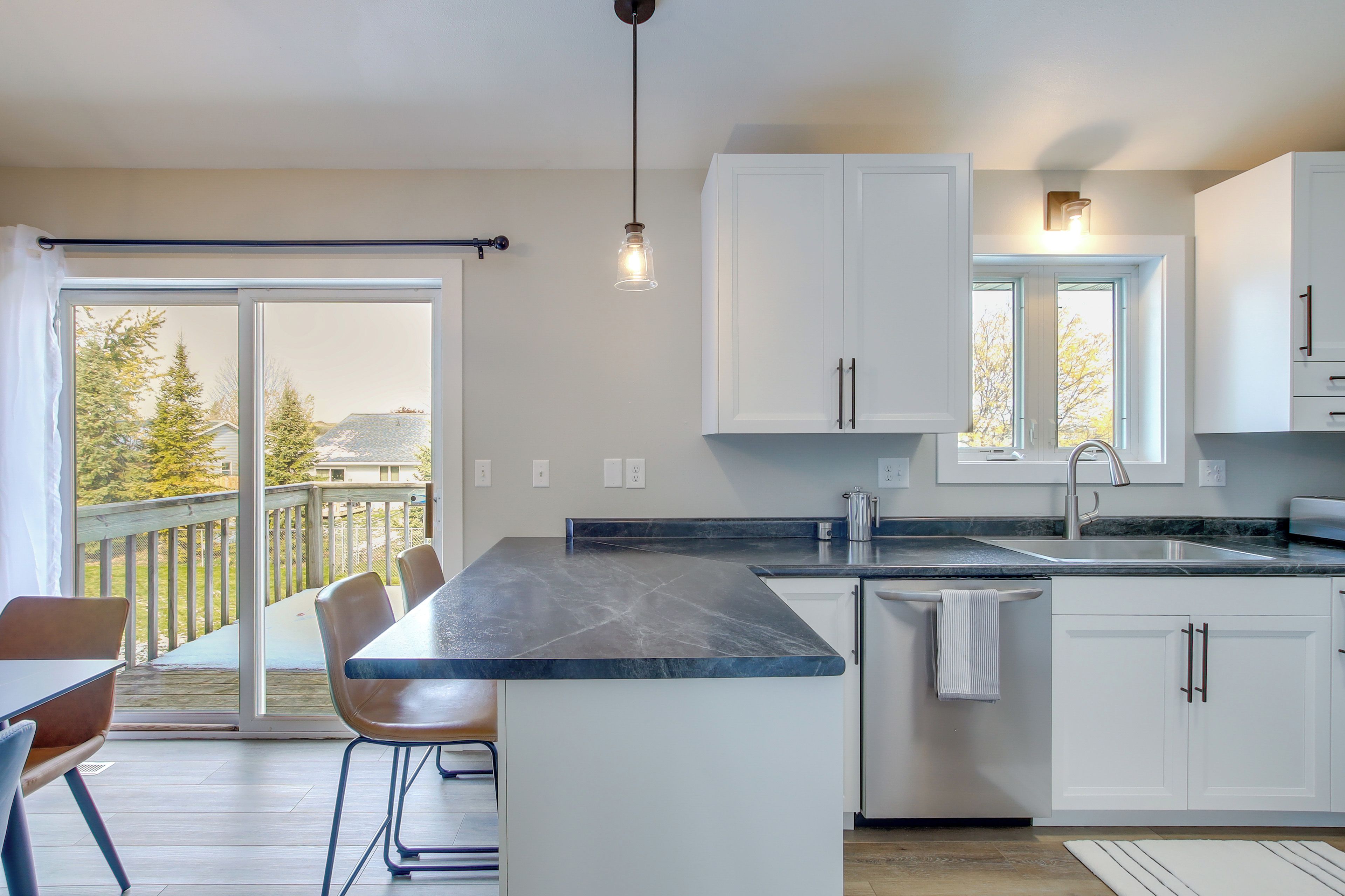 A modern kitchen with a large island, white cabinets, a built-in oven, and a view of a deck.