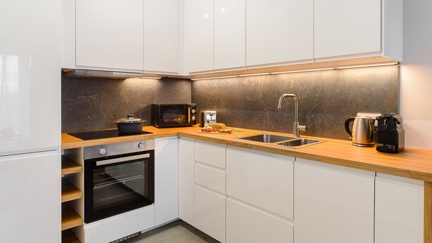 Una cocina moderna con armarios blancos, encimera de madera, horno integrado, microondas, tostadora, fregadero y cafetera.