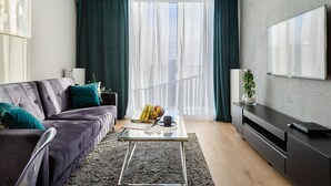 A modern living room with a dark purple sofa, a glass coffee table, and a flat-screen TV on a black stand. - Mokotów Domaniewska 47a (Warsaw)