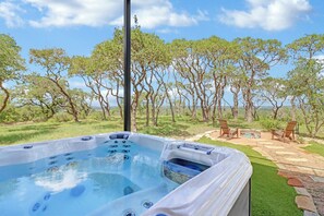 Un bain à remous offrant une vue dégagée sur le paysage environnant, notamment sur les arbres et une terrasse aménagée avec des chaises.