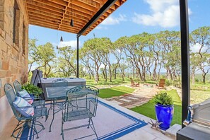 Une terrasse extérieure avec une table et des chaises, un barbecue et une vue sur les arbres et l’herbe.