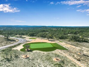 Golfkenttä, jossa on mutkitteleva tie, hiekkabunkkereita ja lippu viheriöllä.
