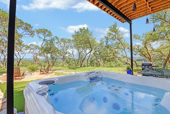 Un bain à remous avec vue sur les arbres et un barbecue à l’arrière-plan.