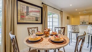 Un coin repas avec une table ronde dressée pour quatre personnes, entourée de chaises. Un tableau encadré est accroché au mur au-dessus de la table.