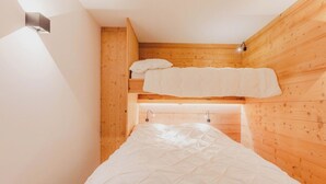 Une petite pièce chaleureuse aux murs en bois, avec un lit superposé et un lit simple.