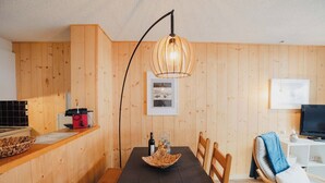 Une pièce aux murs lambrissés, comprenant une table à manger, des chaises, un téléviseur et une lampe.