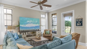 A living room with a large TV, a ceiling fan, and a 'Seas the Day' sign. - Golf Cart ~ Pet Friendly ~ Golf Course View (Miramar Beach)