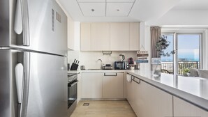 Een moderne keuken met roestvrijstalen apparatuur, lichte houten kastjes en uitzicht op de zee.