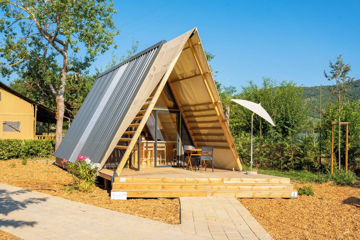 Una estructura de madera triangular con techo inclinado, una terraza de madera y una pequeña mesa con sillas.